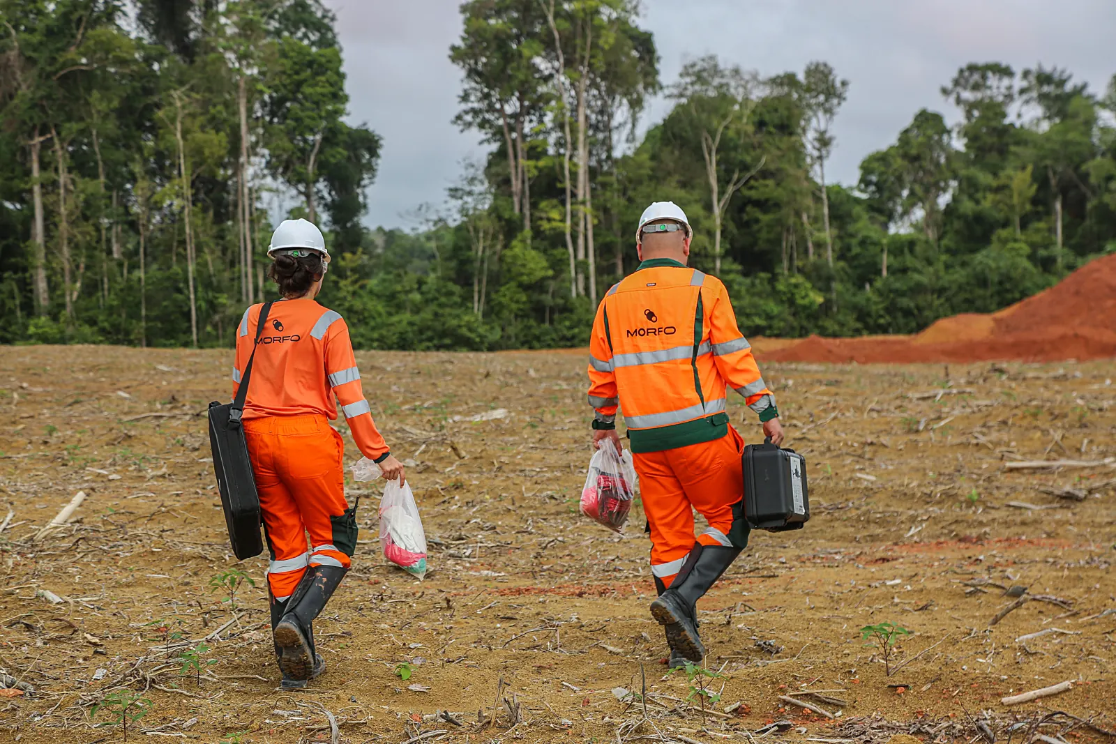 Two MORFO field agents crossing the bare post-bauxite front at Paragominas, sampling kit in hand